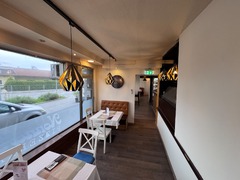 Blick in den hellen und gemütlichen Gastraum von Nonna’s Pizzeria in Seiersberg mit gedeckten Tischen, großen Fenstern und warmer Beleuchtung.